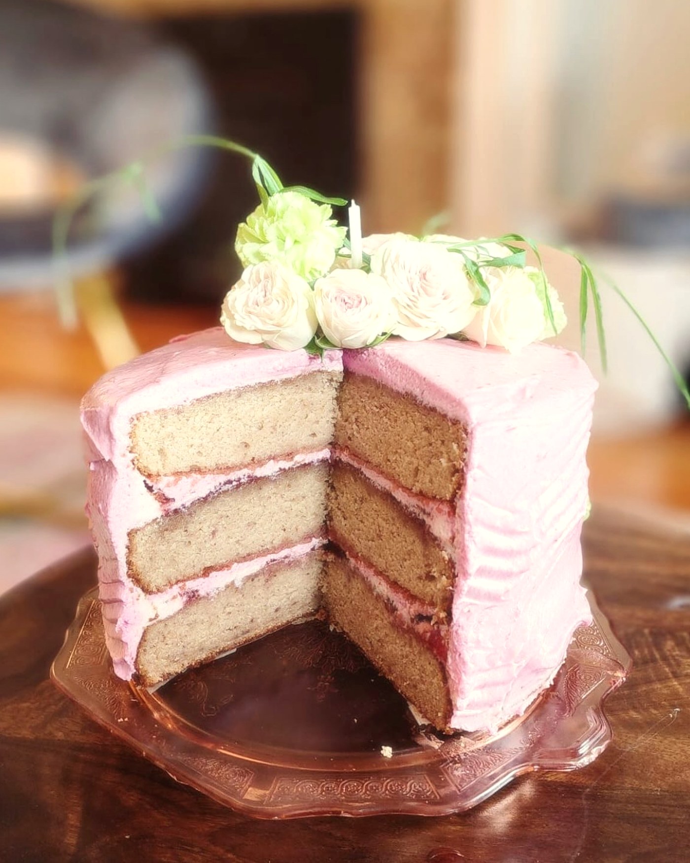 A three-layer pink buttercream cake with jam-filled layers, crowned with garden roses and a single candle